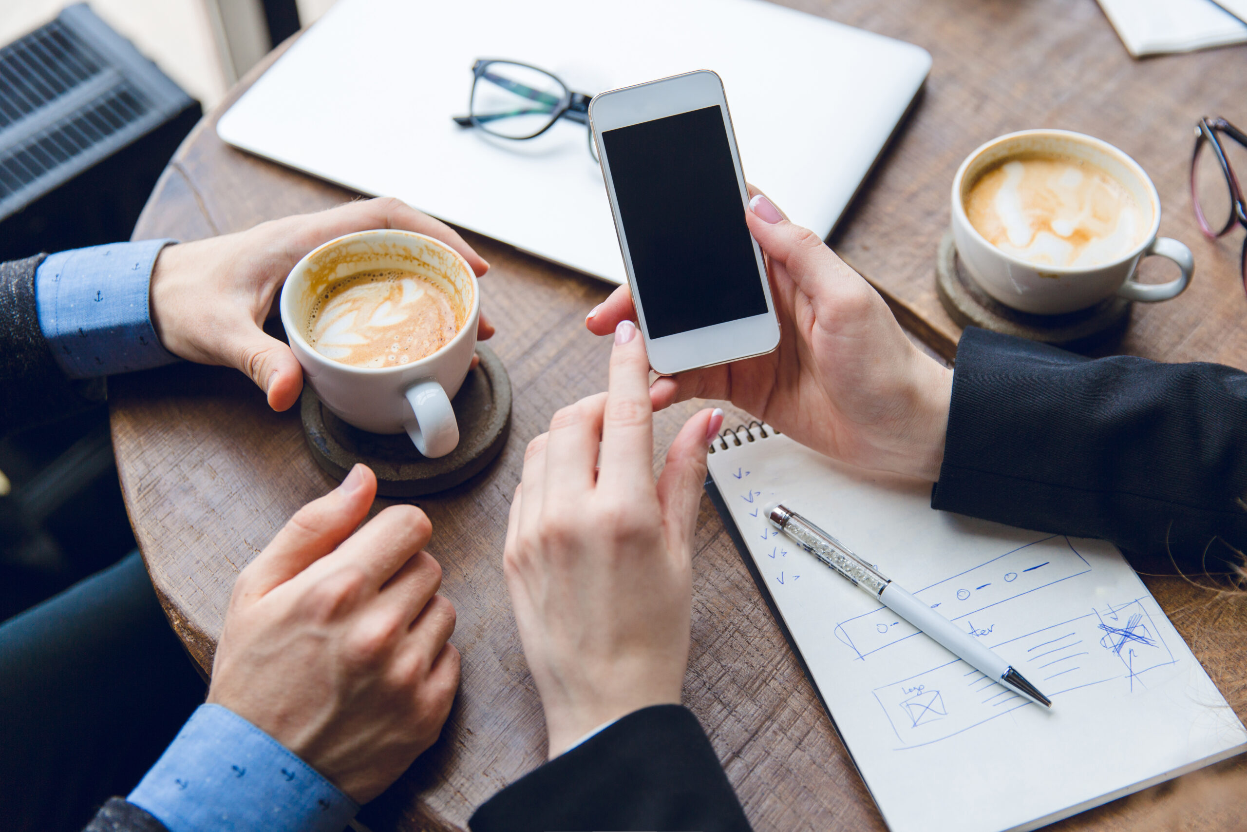 close up white smartphone woman s hands two colleagues sitting coffee table drinking coffee